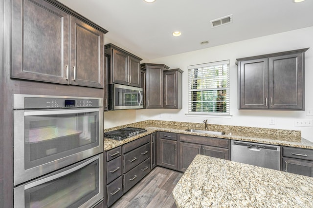 kitchen featuring sink, light wood-type flooring, light stone countertops, and appliances with stainless steel finishes