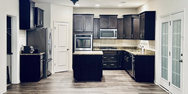 kitchen with a kitchen island, sink, light stone counters, stainless steel appliances, and light hardwood / wood-style flooring