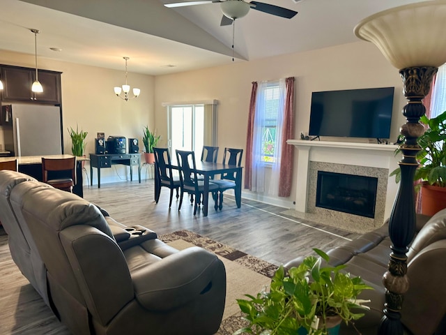 living room with ceiling fan with notable chandelier, vaulted ceiling, a high end fireplace, and light hardwood / wood-style flooring