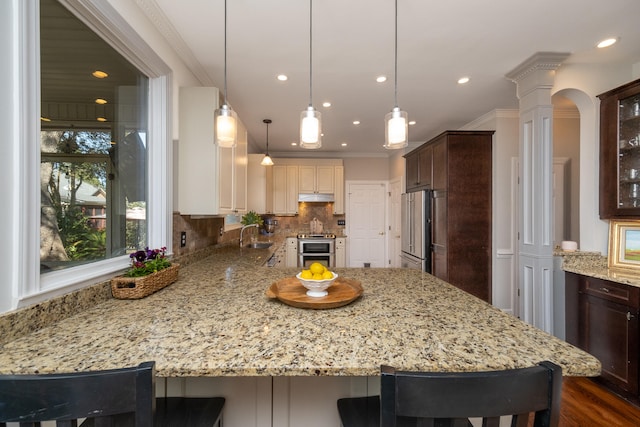 kitchen featuring a kitchen breakfast bar, appliances with stainless steel finishes, ornate columns, and crown molding