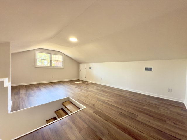 additional living space with dark wood finished floors, vaulted ceiling, baseboards, and visible vents