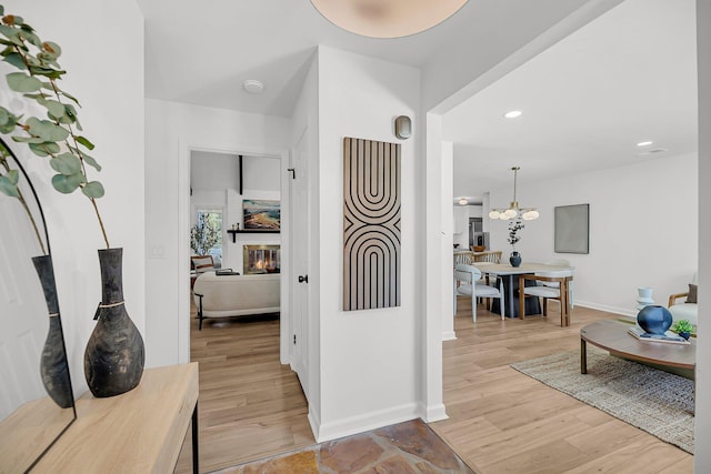 corridor featuring recessed lighting, baseboards, an inviting chandelier, and light wood-style flooring