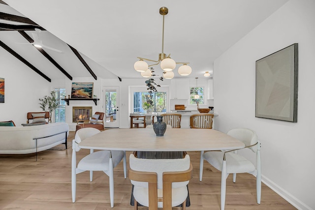 dining space featuring lofted ceiling with beams, light wood-style flooring, plenty of natural light, and a glass covered fireplace