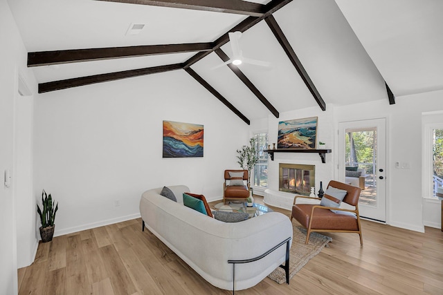 living area with beam ceiling, a glass covered fireplace, light wood-type flooring, and baseboards