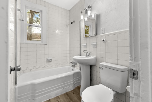 bathroom with tile walls, hardwood / wood-style floors, tiled shower / bath, and toilet