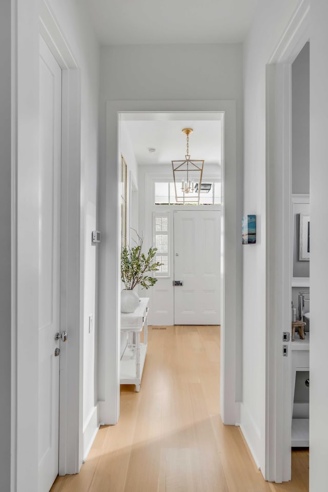 hallway featuring light wood-type flooring and an inviting chandelier