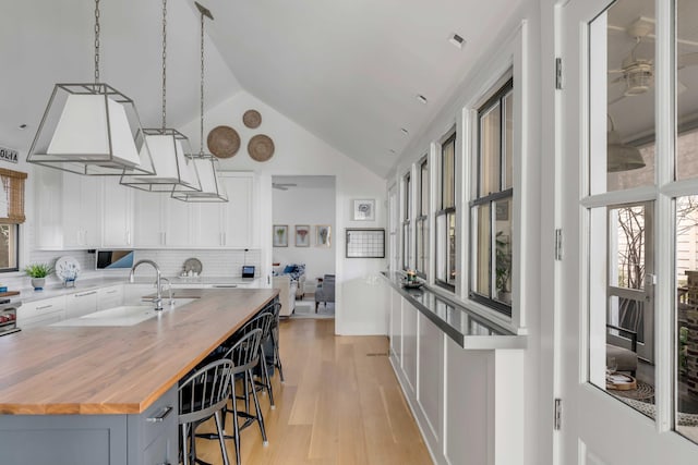 kitchen featuring wood counters, a center island with sink, a breakfast bar area, backsplash, and white cabinets