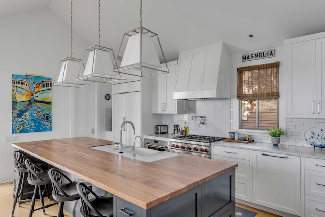 kitchen with white cabinetry, butcher block counters, decorative backsplash, premium range hood, and a center island with sink