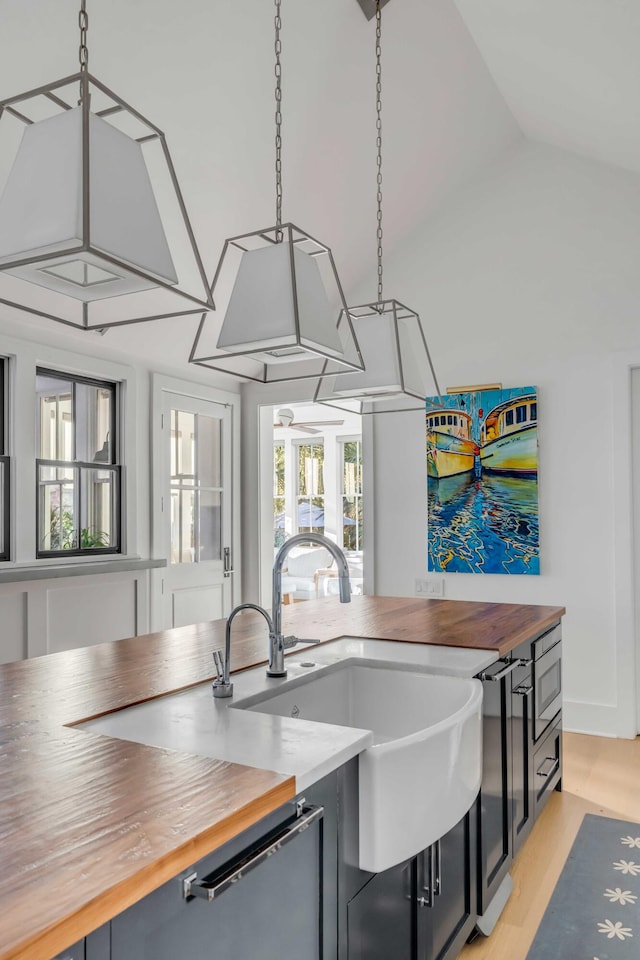 kitchen featuring butcher block counters, stainless steel microwave, decorative light fixtures, vaulted ceiling, and sink