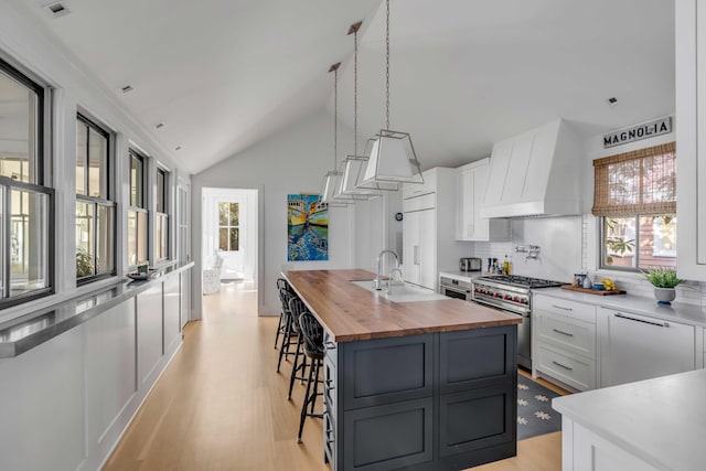 kitchen featuring premium range hood, white cabinetry, stainless steel stove, and decorative light fixtures