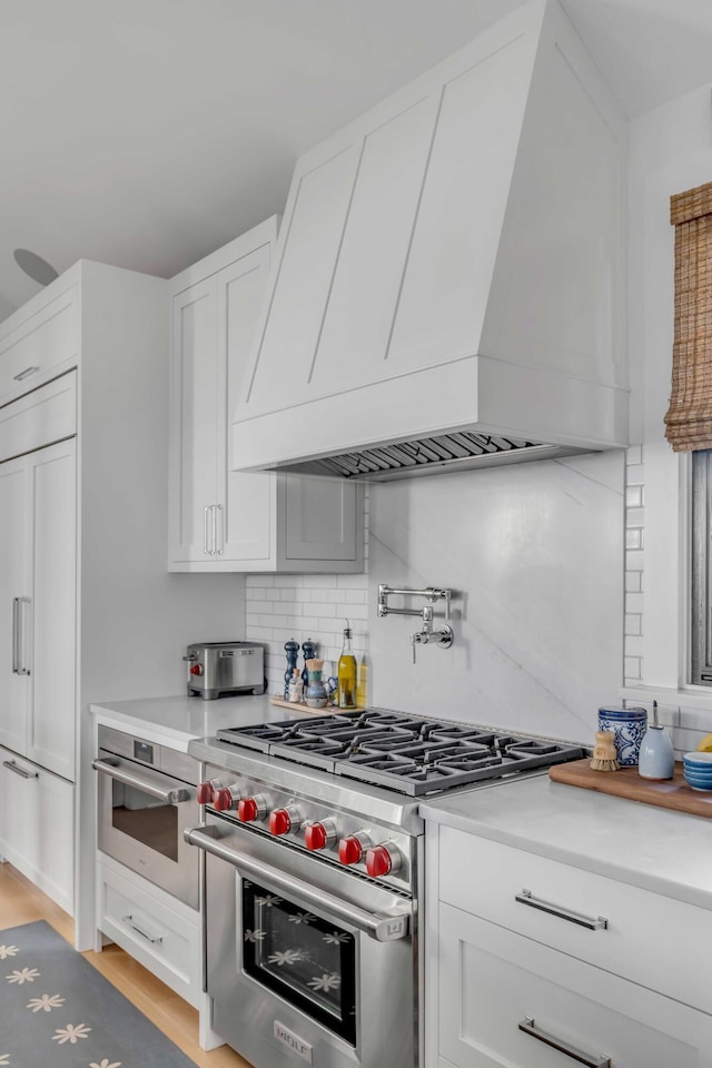 kitchen featuring white cabinetry, decorative backsplash, premium appliances, and custom range hood