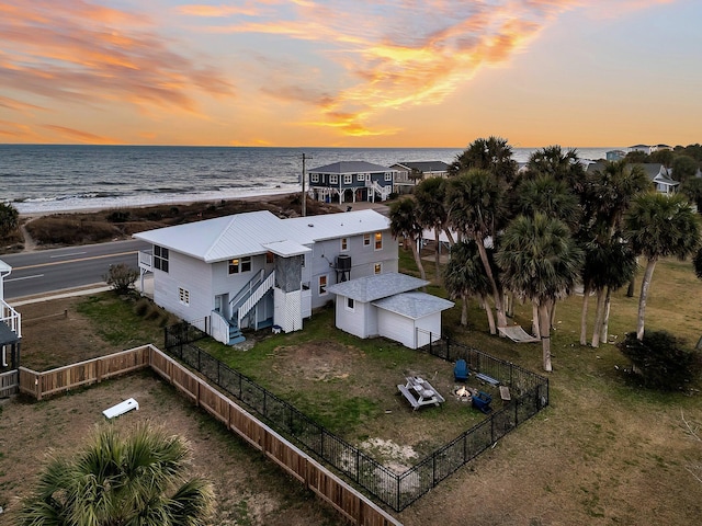 aerial view at dusk featuring a water view and a beach view