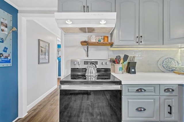 kitchen featuring crown molding, wood-type flooring, electric range, gray cabinets, and backsplash