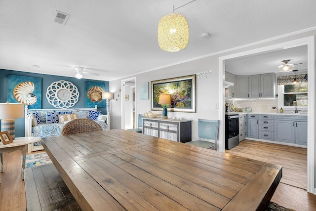 dining room featuring sink, light hardwood / wood-style flooring, ornamental molding, and ceiling fan