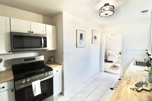 kitchen featuring white cabinets, wood counters, sink, and appliances with stainless steel finishes