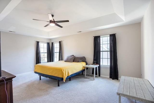 carpeted bedroom featuring multiple windows, a raised ceiling, and ceiling fan