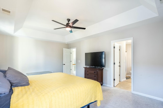 carpeted bedroom with a raised ceiling, connected bathroom, and ceiling fan