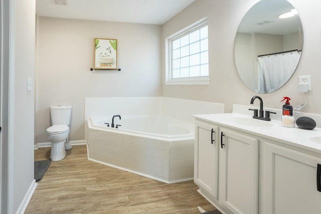 bathroom featuring a relaxing tiled tub, wood-type flooring, toilet, and vanity