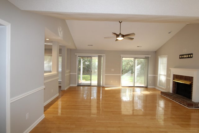 unfurnished living room with ceiling fan, vaulted ceiling, light wood-type flooring, and a brick fireplace