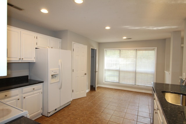 kitchen with white cabinets, light tile patterned flooring, white refrigerator with ice dispenser, and sink