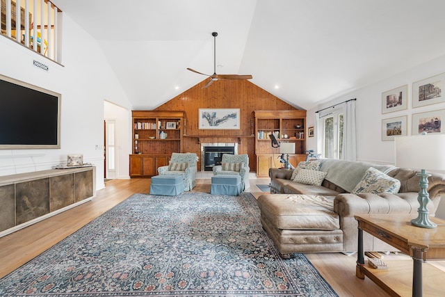 living room featuring ceiling fan, lofted ceiling, light wood-type flooring, and wood walls