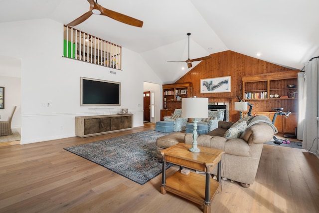 living room with vaulted ceiling, light wood-type flooring, wooden walls, and ceiling fan