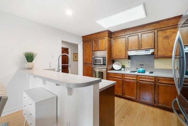 kitchen featuring appliances with stainless steel finishes, sink, light wood-type flooring, and kitchen peninsula