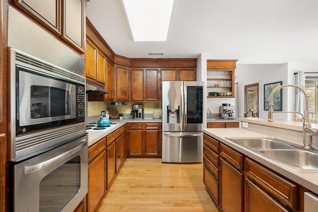 kitchen with appliances with stainless steel finishes, sink, and light hardwood / wood-style flooring