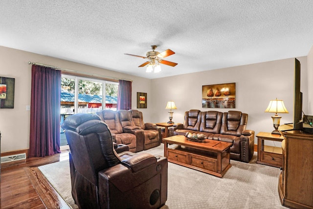 living room with ceiling fan, light wood-type flooring, and a textured ceiling