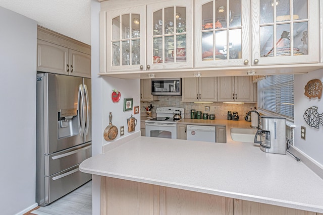 kitchen featuring kitchen peninsula, stainless steel appliances, light brown cabinets, tasteful backsplash, and sink