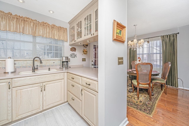 kitchen with a notable chandelier, light wood-type flooring, a textured ceiling, pendant lighting, and sink