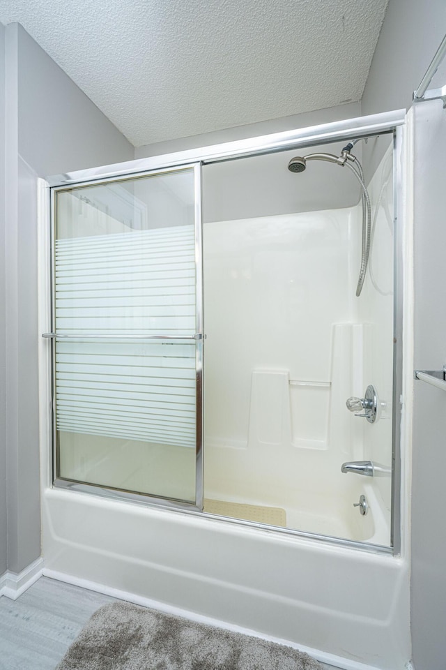 bathroom with wood-type flooring, a textured ceiling, and shower / bath combination with glass door