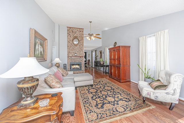 living room featuring ceiling fan, hardwood / wood-style floors, and a brick fireplace