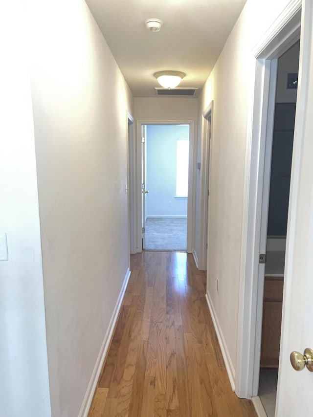 corridor featuring light wood-style flooring, visible vents, and baseboards