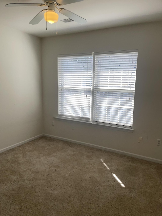 empty room with carpet floors, a ceiling fan, visible vents, and baseboards