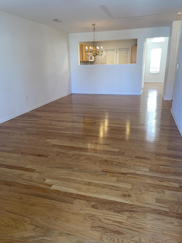 unfurnished room with baseboards, visible vents, a chandelier, and wood finished floors