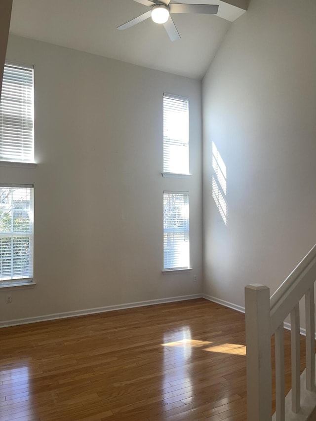 spare room with high vaulted ceiling, baseboards, plenty of natural light, and hardwood / wood-style floors