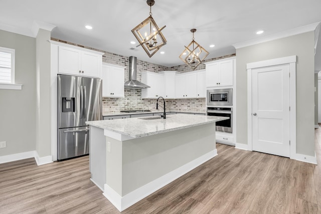 kitchen featuring a kitchen island with sink, sink, hanging light fixtures, wall chimney exhaust hood, and stainless steel appliances