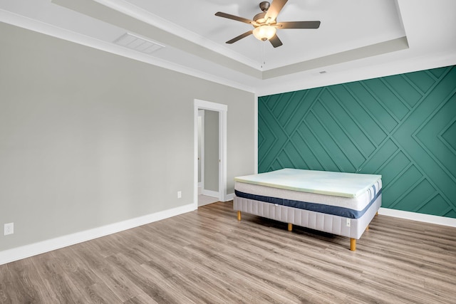 unfurnished bedroom featuring a raised ceiling, ceiling fan, crown molding, and light wood-type flooring