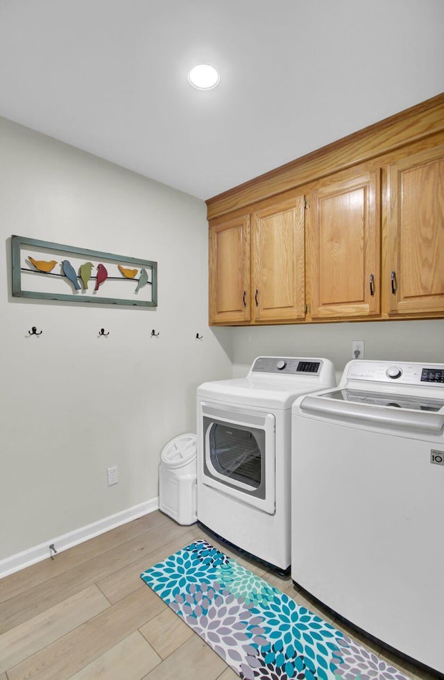 laundry area featuring washing machine and clothes dryer, light hardwood / wood-style floors, and cabinets