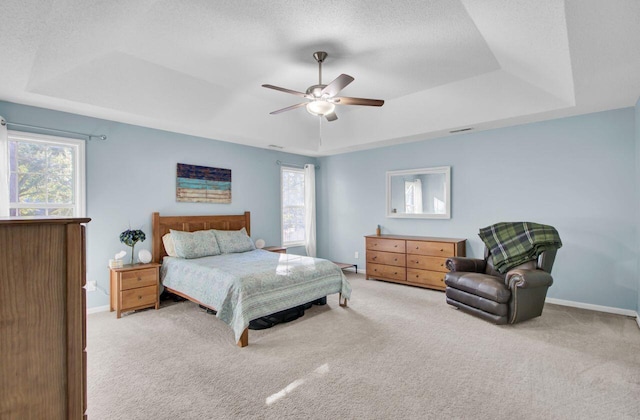 carpeted bedroom with a textured ceiling, ceiling fan, and a raised ceiling