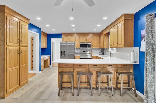 kitchen with stainless steel appliances, a kitchen breakfast bar, backsplash, kitchen peninsula, and light wood-type flooring