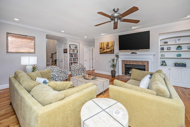 living room with built in shelves, a fireplace, ornamental molding, and light wood-type flooring