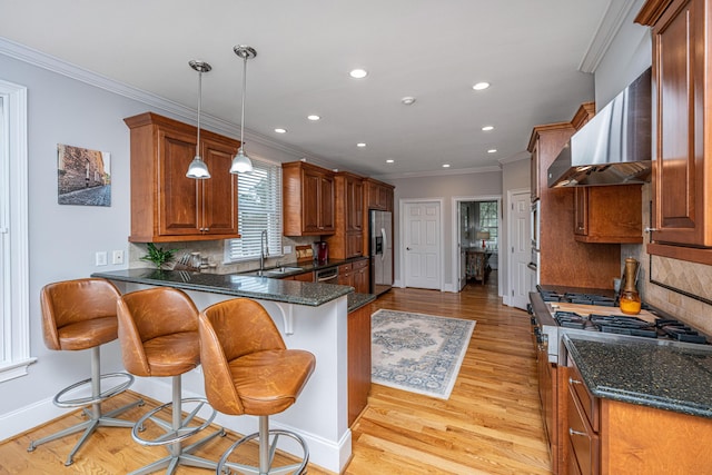 kitchen featuring wall chimney exhaust hood, sink, a breakfast bar area, appliances with stainless steel finishes, and pendant lighting