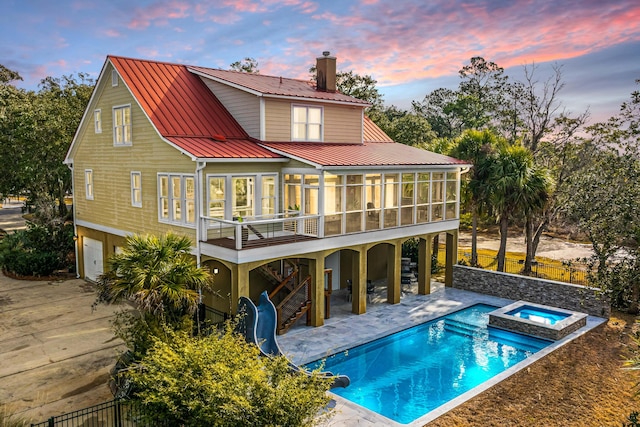 back house at dusk featuring a pool with hot tub, a patio area, a sunroom, and a balcony