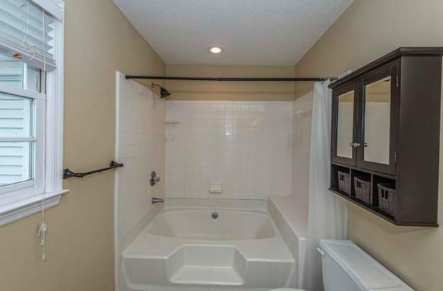 bathroom featuring tiled shower / bath combo, toilet, and a textured ceiling