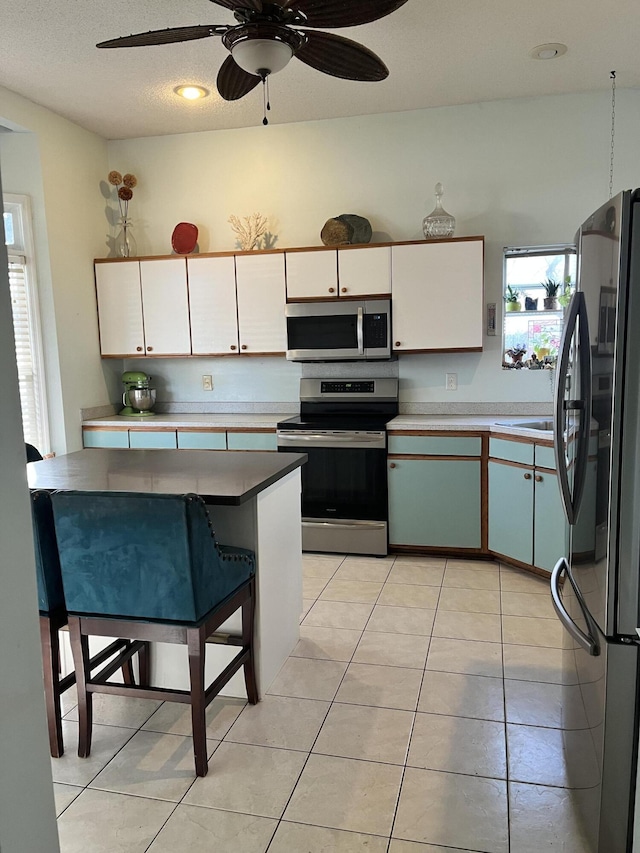 kitchen with appliances with stainless steel finishes, a textured ceiling, ceiling fan, light tile patterned floors, and white cabinetry