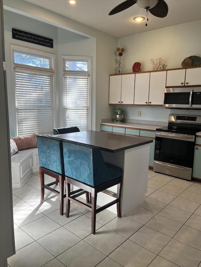 kitchen with white cabinetry, a center island, ceiling fan, a kitchen breakfast bar, and appliances with stainless steel finishes