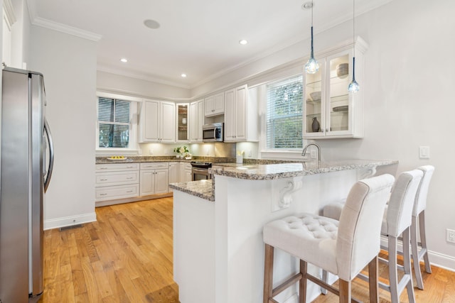 kitchen featuring stainless steel appliances, kitchen peninsula, hanging light fixtures, stone counters, and light wood-type flooring