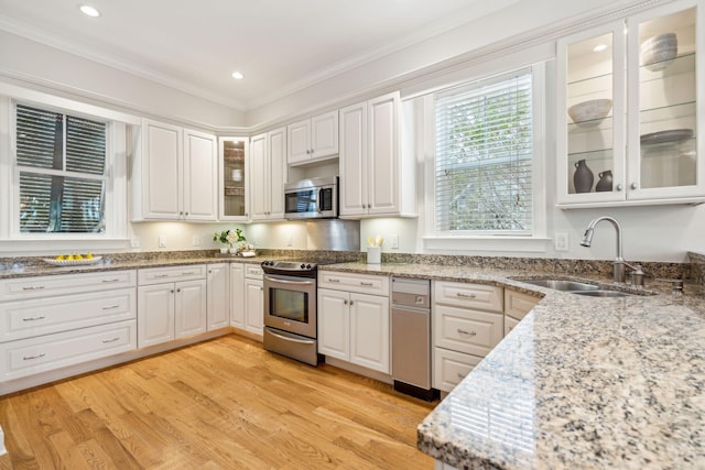 kitchen featuring white cabinetry, sink, appliances with stainless steel finishes, ornamental molding, and light wood-type flooring